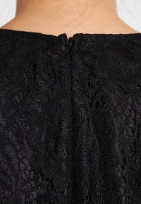 Tissu de robe en dentelle noire avec un motif floral texturé. Équipée d'une fermeture éclair au dos. Tissu lisse et délicat, avec des sections transparentes.