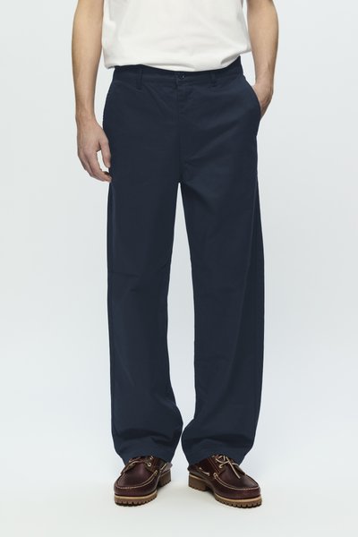 Pantalons bleu marine à jambes larges en coton, dotés de poches latérales et d'un devant plat, associés à des chaussures en cuir marron.