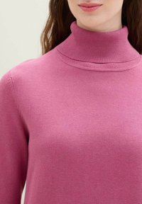 Dopasowany sweter typu golf w miękkim różowym dzianinie. Posiada prążkowany kołnierz i gładką fakturę, z minimalnymi detalami szwów.