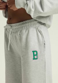 Szare dresowe spodnie z elastycznym paskiem, sznurkiem do ściągania oraz kolorowym logo "B" w zielonym i różowym kolorze na lewej nodze. Miękka faktura.