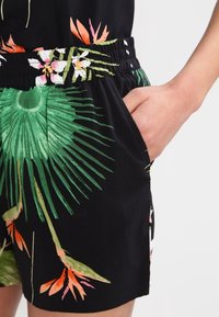 Czarne szorty w kwiatowy wzór z zielonymi, różowymi i pomarańczowymi akcentami. Elastyczna talia i podkreślony detal bocznej kieszeni.
