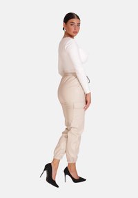 Weißes langärmliges Crop-Top, beige Cargo-Hosen mit elastischen Bündchen und schwarzen Stiletto-Absätzen. Die Hosen haben seitliche Taschen und einen Kordelzug.