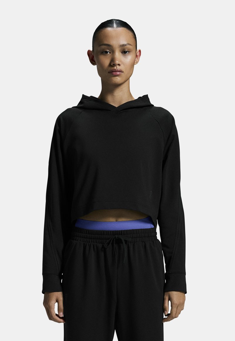 Fekete cropped kapucnis pulóver, hosszú ujjú, texturált anyagból készült. Fekete joggerekhez párosítva, kék derékrésszel.