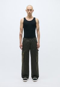 Μαύρα κοντομάνικα μπλουζάκια, ελαιόχρωμο cargo παντελόνι με πολλές τσέπες και κίτρινο φερμουάρ, χαλαρή εφαρμογή, υφή υφάσματος, φοριούνται με μαύρα αθλητικά παπούτσια.