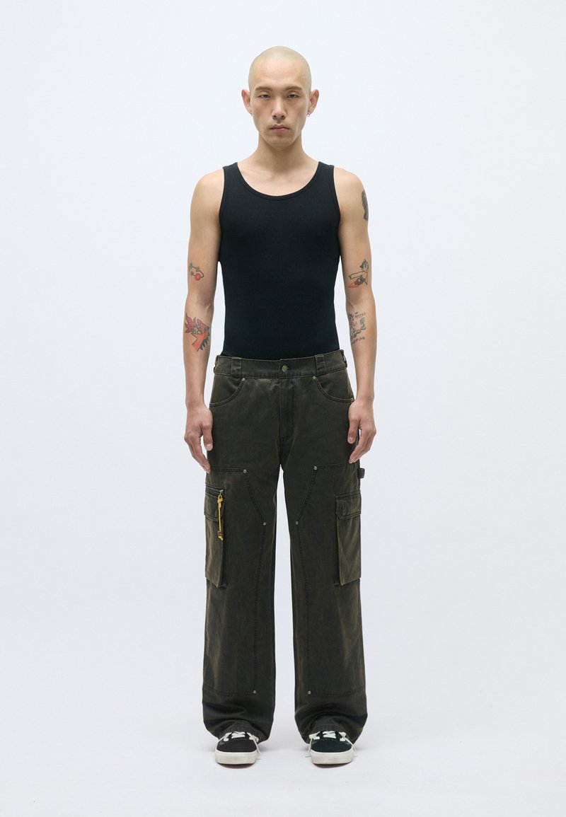 Μαύρα κοντομάνικα μπλουζάκια, ελαιόχρωμο cargo παντελόνι με πολλές τσέπες και κίτρινο φερμουάρ, χαλαρή εφαρμογή, υφή υφάσματος, φοριούνται με μαύρα αθλητικά παπούτσια.