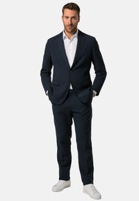 Completo blu navy con giacca su misura a due bottoni, abbinato a pantaloni su misura e camicia bianca; indossato con sneakers bianche.