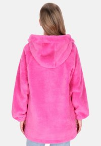 Růžová fleecová mikina s měkkou texturou, volným střihem a velkou kapucí. Má široké rukávy a zaoblený spodní lem. Zobrazen pohled zezadu.