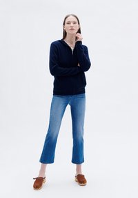 Felpa con zip color navy, jeans azzurri a vita media e zoccoli marroni. Tessuto morbido, vestibilità rilassata e lunghezza dei pantaloni accorciata con un orlo leggermente sfilacciato.