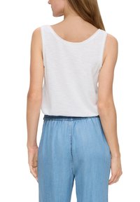 Witte mouwloze top met een gladde textuur en ronde halslijn, gecombineerd met lichtblauwe denim broek met een elastische tailleband.