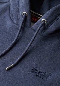 Felpa blu navy con una finitura testurizzata, dotata di punte in argento per i lacci e di un logo ricamato sul petto.