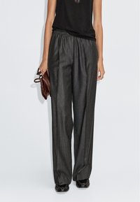 Zwart en grijs gestreepte wijde broek met elastische tailleband, gecombineerd met een zwart top en een bruine tas. Getextureerde stof.