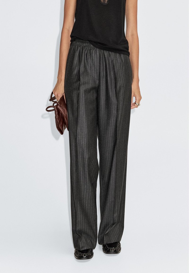 Zwart en grijs gestreepte wijde broek met elastische tailleband, gecombineerd met een zwart top en een bruine tas. Getextureerde stof.