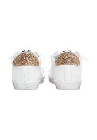 Un paio di sneakers bianche con accenti di glitter dorato sul tallone, viste da dietro, mostrano i lacci e le suole leggermente usurate.