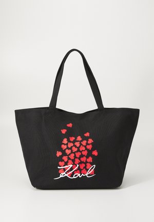 Black tote bag with red heart pattern and white "Karl" text. Made of durable fabric, features wide handles for easy carrying.