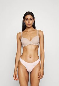 Beige vadderad behå med justerbara axelband och matchande ljusrosa bikini med låg midja. Mjuk textur och minimalistisk design utan synliga dekorationer.