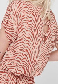 Top de manga corta en beige con un patrón de rayas de cebra rojas; cuenta con un detalle cortado en la parte posterior con tirantes cruzados. Material suave y ligero.