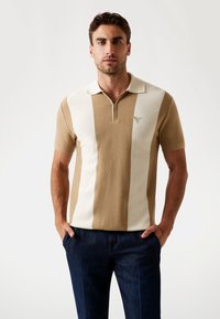 Tricou polo din tricot, cu dungi alternante de culoare bej deschis și crem, guler cu fermoar, mâneci scurte și un mic logo pe piept.