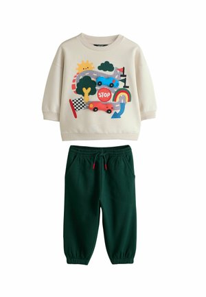 Cremelanger Pullover mit buntem Straßen- und Autodesign, kombiniert mit dunkelgrünen elastischen Jogginghosen mit Bündchen am Bund und den Knöcheln.