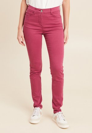 Jean en denim rose ajusté taille haute avec cinq poches et fermeture à bouton métallique, associé à des baskets blanches et beiges.