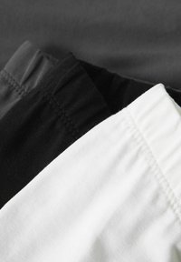 Trois paires de shorts en blanc, noir et gris. Le tissu est en coton doux avec des ceintures élastiques et des détails de couture soignés.