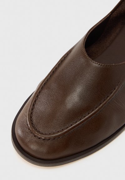 Chaussure mocassin en cuir marron avec bout arrondi, coutures apparentes et texture lisse. Design minimaliste avec semelle en caoutchouc légère.