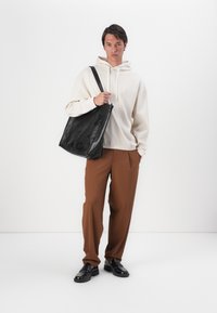 Crème hoodie met een elastische zoom, losse bruine broek en een zwarte leren schoudertas. Zwarte schoenen maken de outfit compleet.