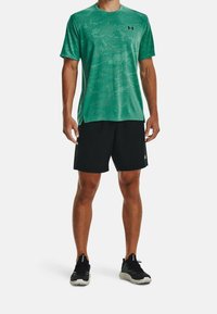 Grön kortärmad träningsskjorta med ett subtilt mönster, kombinerad med svarta shorts. Outfiten kompletteras av svarta löparskor.