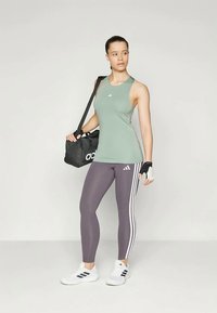 Canottiera verde senza maniche, leggings grigi con strisce bianche, borsa da palestra nera, sneakers bianche e guanti neri. Design atletico semplice.