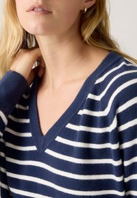 Suéter a rayas azul marino y blanco con diseño de cuello en V, fabricado con material suave. Cuenta con puños acanalados y un corte holgado.