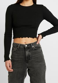 Schwarzes, geripptes Cropped-Top mit langen Ärmeln, das einen gewellten Saum und eine figurbetonte Passform aufweist, kombiniert mit hochgeschnittenen, ausgewaschenen schwarzen Jeans.