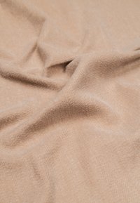 Tela beige texturizada con una apariencia suave y cálida, mostrando pliegues suaves y un sutil patrón de espiga. Adecuada para diversos usos.