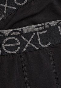 Schwarze Herrenunterwäsche mit einem breiten, elastischen Bund, auf dem "next" in Grau steht, und einem glatten Stoff mit subtiler Textur.