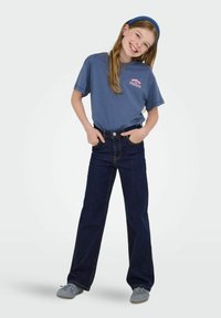 Modra bombažna majica s kratkimi rokavi in roza napisom "MAREC" na prsih, v kombinaciji z temno svetlim širokima hlačami z visokim pasom.