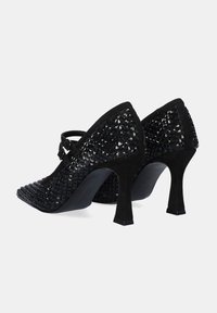 Zapatos de tacón negro con un upper de tejido texturizado, punta afilada y acentos de doble hebilla en el empeine.