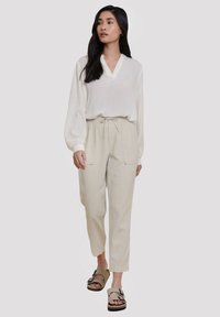 Lätt, krämfärgad blus med V-ringning och långa, puffärmar; kombinerad med mjuka, beige tapered byxor med elastisk midja och fickor.