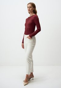 Bordeaux kleurige longsleeve bodysuit met geribbelde textuur, gecombineerd met witte rechte jeans en beige hakken met slingback. Eenvoudig ontwerp, geen zichtbare patronen.