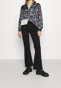 Jeans neri a campana abbinati a una blusa a stampa floreale con scollo a V e maniche lunghe. Una borsa a tracolla bianca e di tessuto completa il look.