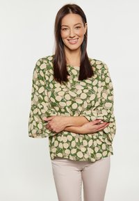 Blusa con motivo verde e avorio, maniche a campana a tre quarti, abbinata a pantaloni fitted beige chiaro. Tessuto morbido, design casual.