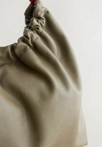 Sac à main en cuir vert avec un sommet froncé, présentant une texture lisse et un éclat subtil. Il est doté d'une poignée rouge robuste.