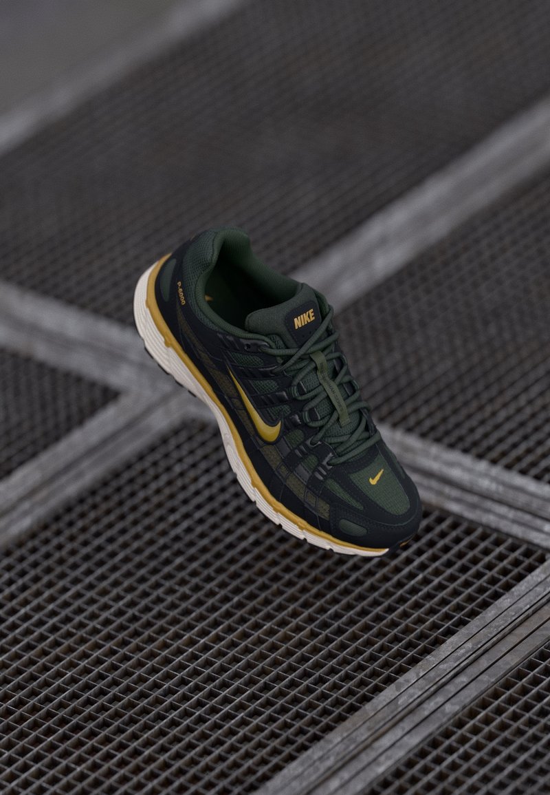Baskets Nike vert foncé et noir avec des accents jaunes sur une surface en grille métallique, montrant la vue latérale et supérieure de la chaussure.