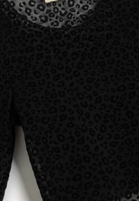 Zwarte panterprint top met een textuurstof en een abstract patroon. Ronde halslijn en korte mouwen, afgewerkt met een doorschijnende overlay.