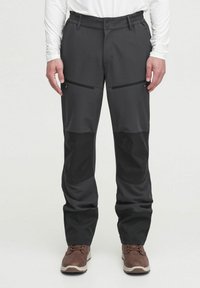 Pantalones exteriores negros con una textura suave, que cuentan con dos bolsillos frontales con cremallera y paneles en contraste en la parte baja de las piernas.
