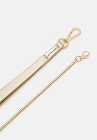 Sangle de couleur dorée avec une finition métallique lisse et des éléments métalliques. Caractérisée par un design plat et des fermoirs à crochet.