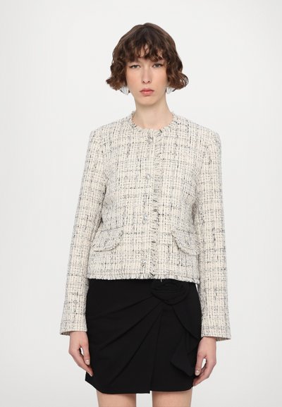 Veste en tweed texturé crème et noir avec un col rond, des boutons à l'avant, et deux poches à rabat, associée à une jupe plissée noire.