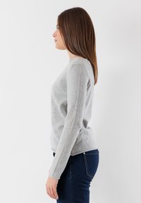 Maglione grigio chiaro a maniche lunghe realizzato in materiale morbido, con scollatura rotonda, forma aderente e una leggera trama. Indossato con jeans blu scuro.