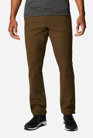 Braune technische Hosen mit geradem Schnitt, verstärkten Kniepaneelen und seitlichen Reißverschlusstaschen, kombiniert mit schwarzen Sportschuhen mit weißen Sohlen.