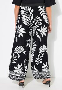 Černé kalhoty s širokými nohavicemi a bílým květinovým vzorem. Elastický pas, vzorovaný lem na spodním okraji, lehká tkanina a volný střih.
