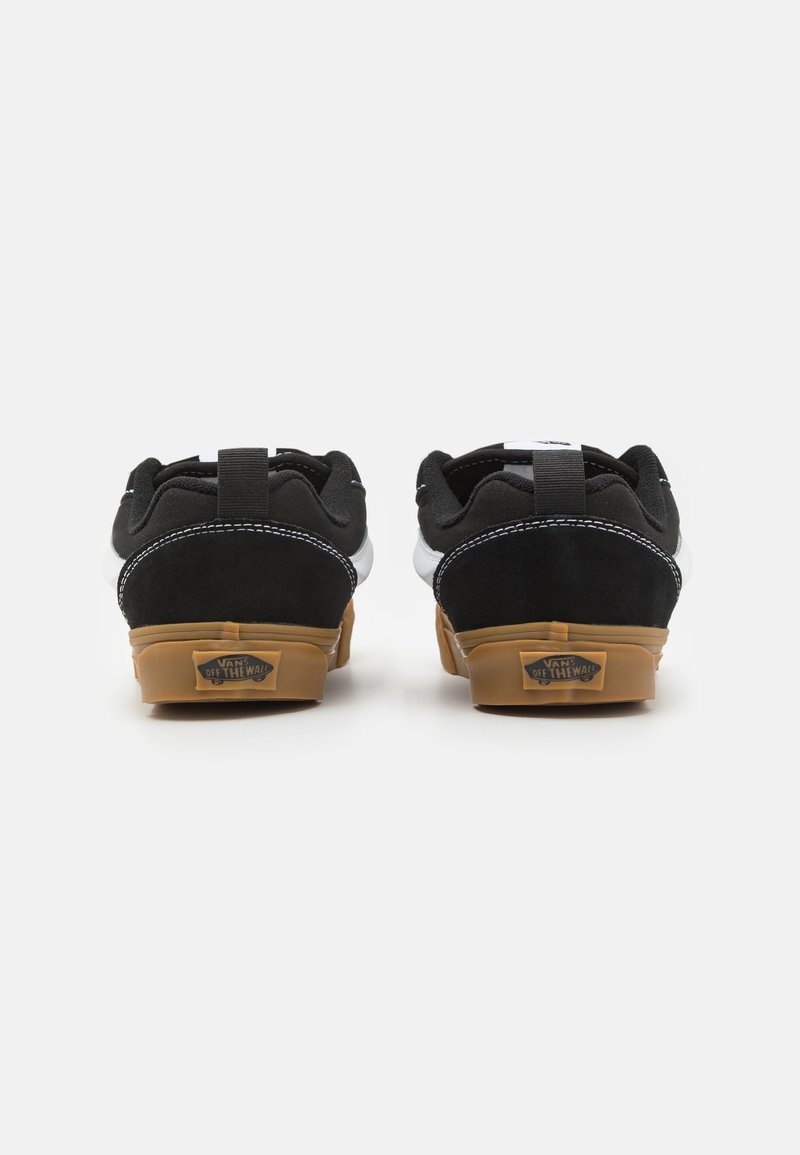 Scarpe sportive in bianco e nero con tomaia in suede e tela, colletto imbottito e suola in gomma con dettagli del logo.