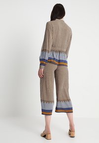 Braun gemustertes Zweiteiler-Outfit mit einer lockeren Bluse in Blau- und Orangestreifen sowie 7/8-Hosen. Hergestellt aus leichtem Stoff.