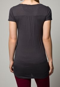 Grå kortärmad topp med rundad halsringning, detaljer med rynkning bak och en något förlängd nederkant. Slät tygkvalitet och figurnära passform.